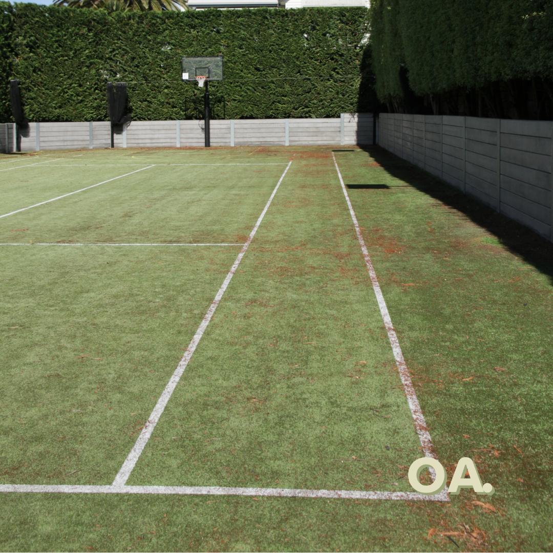 The same walled grass court before, worn and dirty with faded lines