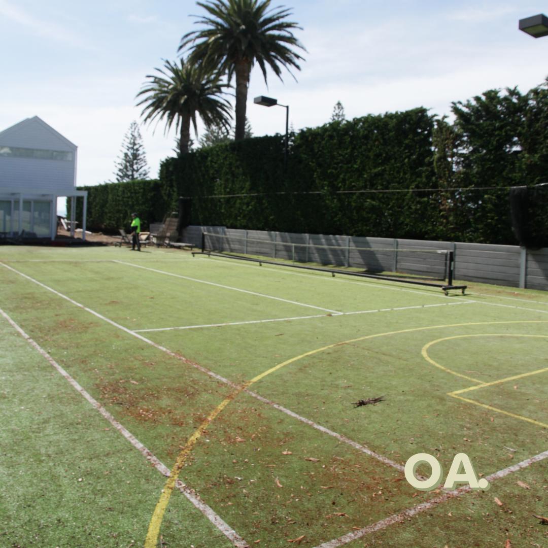 The same walled grass court before, worn and dirty with faded lines